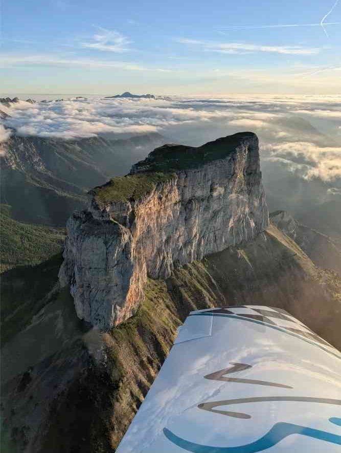 Vue aérienne d’un plateau rocheux spectaculaire entouré de montagnes et de nuages, depuis un avion léger.